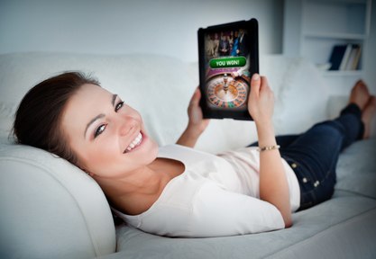 Happy woman lying on couch and gambling on tablet at home in living room